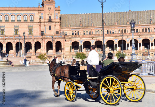 A sunny day at Plaza de Espana, tourists visiting the famous square, a horse-drawn carriage passing by in foreground