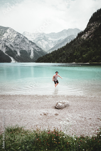 junger mann mit Hut und Tank-Top steht im Wasser des Plansees