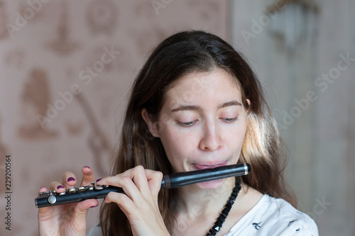 A gorgeous young woman sitting and playing the flute piccolo