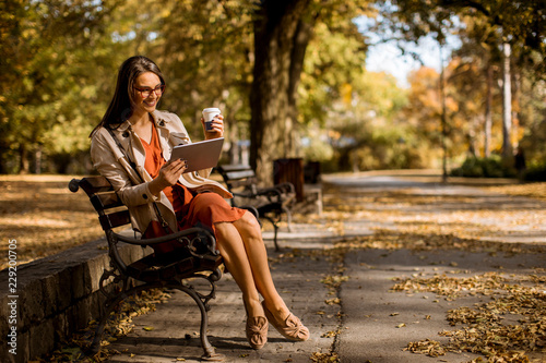 Young woman drinks coffee and using digital tablet in the park