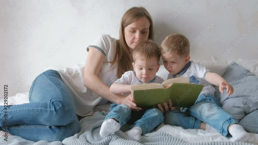 Family mom and two twin brothers toddlers read books laying on the bed. Family reading time. Family mom and two twin brothers toddlers read books laying on the bed. Family reading time.