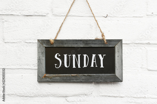 Obraz na plátně Hello sunday weekend text on hanging board white brick outdoor wall
