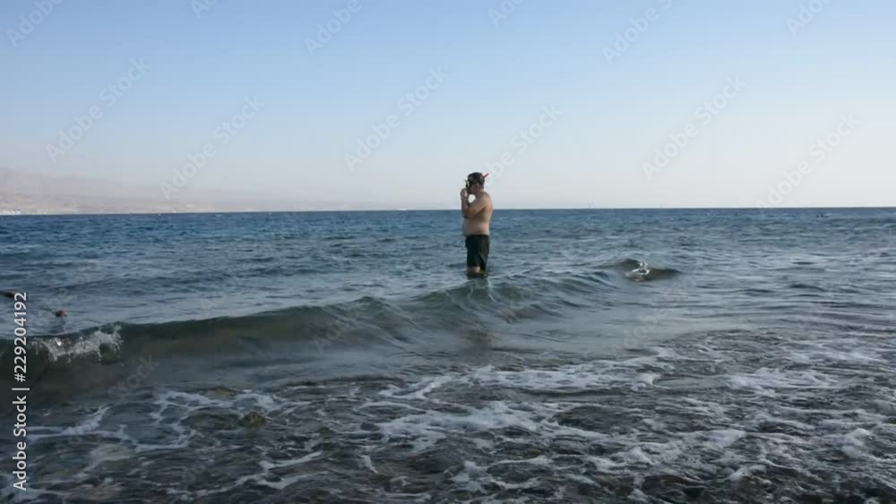 Fat man at the rocky beach entering the sea with mask and snorkel Fat man at the rocky beach entering the sea with mask and snorkel
