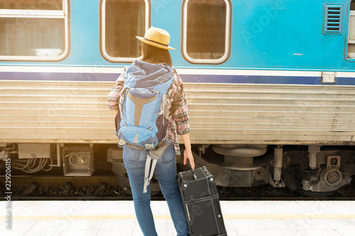 Asia woman Traveller walking and Towing the luggage over the motion blurred of train running at the train station, Travel and lifestyle concept