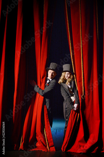 Actor and actress in tuxedos close the theater curtain