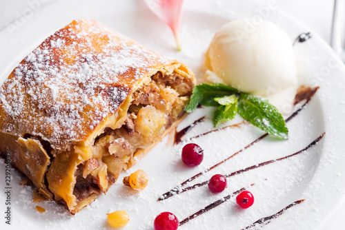 Apple strudel with vanilla ice cream and mint and berries on white plate, close up photo