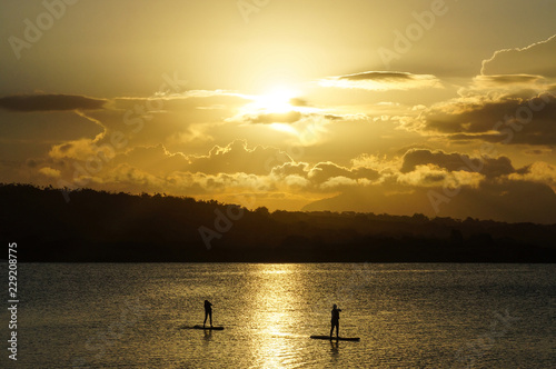 two women practicing stand up paddle on the lagoon at sunset