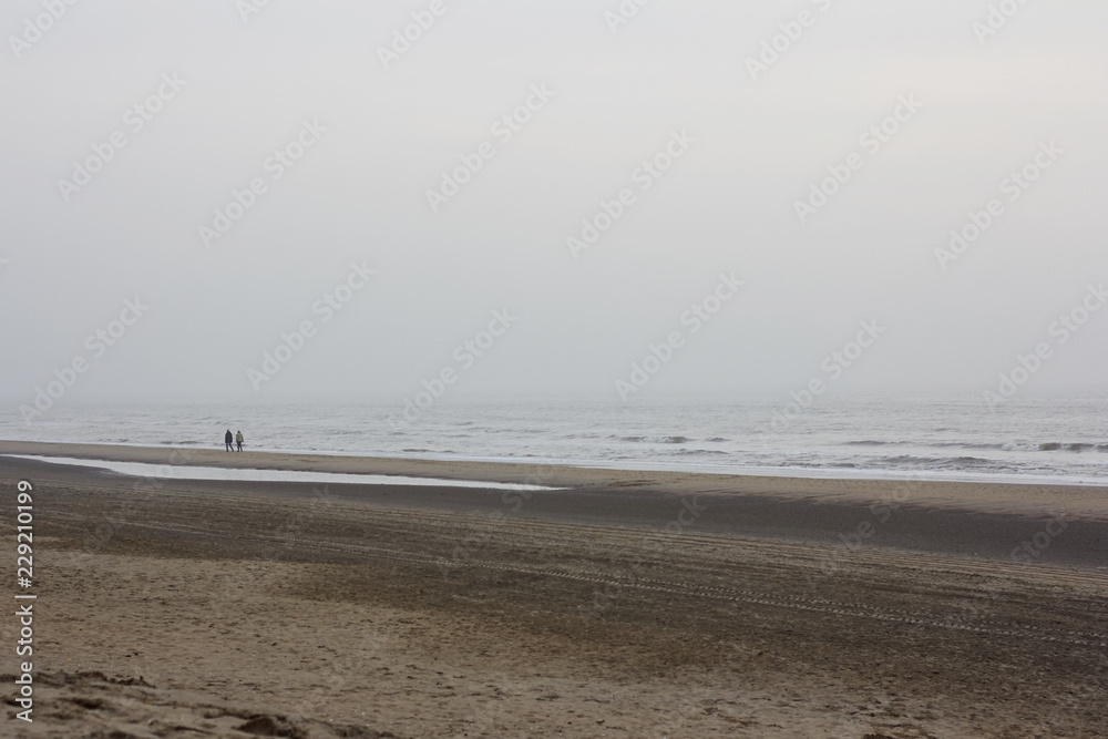 Silhouettes of two people walking along the cold winter shore of the north sea at sunset Silhouettes of two people walking along the cold winter shore of the north sea at sunset