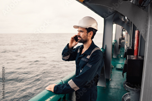 Marine Deck Officer or seaman on deck of vessel or ship . He is speaking on the mobile cell phone photo