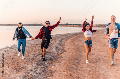Group of young hipster friends on beach running together during sunset. Freedom and friendship concept