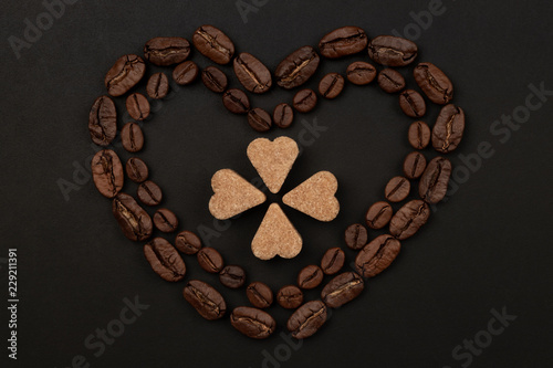 Roasted coffee beans placed in a shape of heart on black background with brown sugar