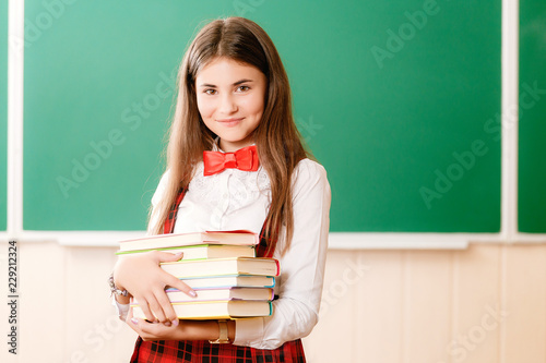 beautiful young school girl in school uniform standing with books in her hands