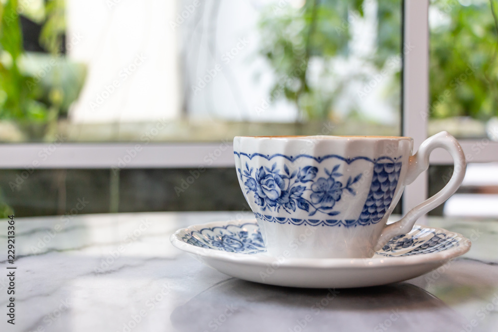 Coffee milk in a cup, rose patterned ceramic cup, on marble table in the morning light. Coffee milk in a cup, rose patterned ceramic cup, on marble table in the morning light.
