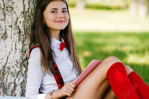 Quadro su tela young schoolgirl in school uniform sitting on the grass under a tree with books
