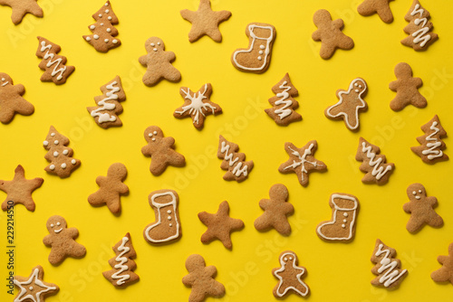 Homemade christmas cookies on yellow background. Pattern of gingerbread men, snowflake, star, fir-tree, boot shapes. New year concept