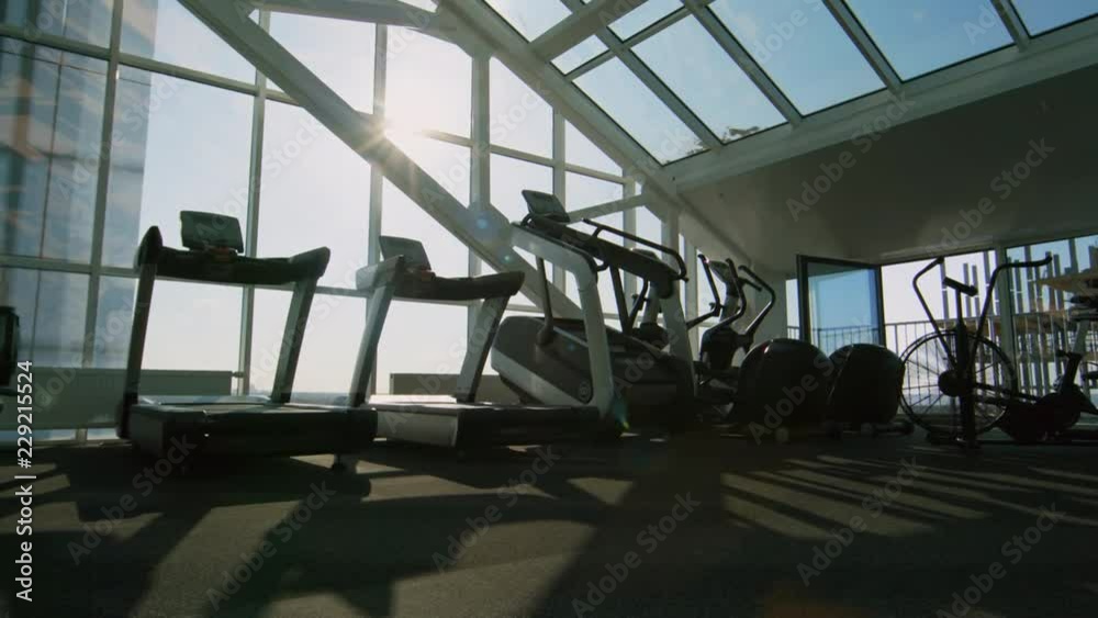 PAN of cardio machine standing in empty gym with panoramic windows and roof PAN of cardio machine standing in empty gym with panoramic windows and roof