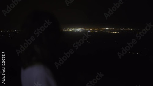 Woman on high mountain watching lights of towns at night in Mallorca, Spain