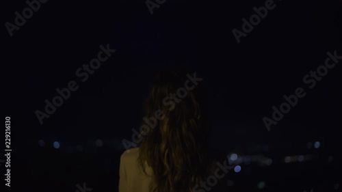 Woman on high mountain at night with city lights in background in Mallorca, Spain