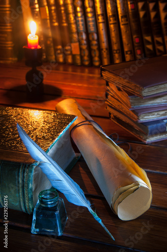 Quill pen and a rolled papyrus sheet on a wooden table with old books