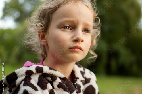 Portrait of a beautiful curly blue-eyed girl sitting on a background of green trees. Vacation in the village.