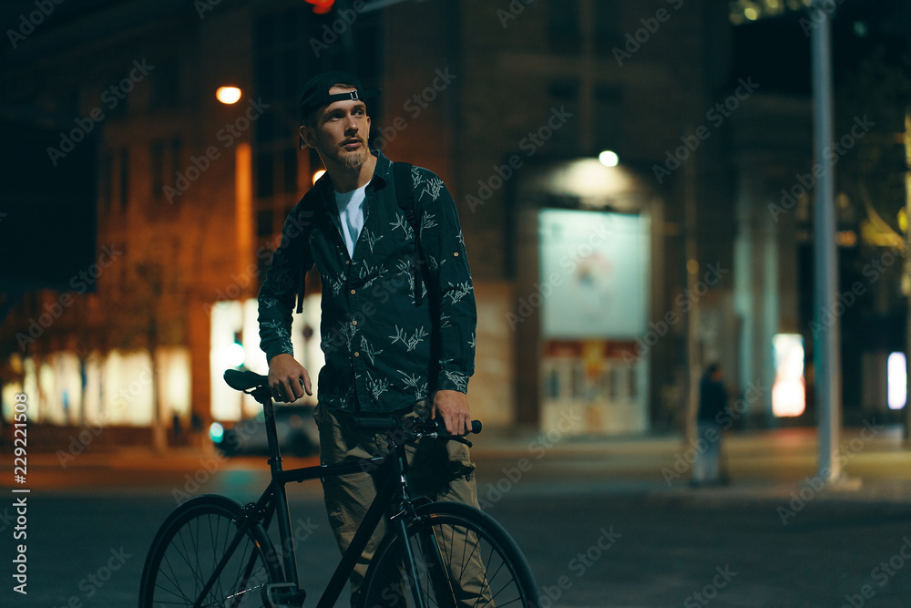 Fototapeta premium Cyclists standing on the road aside his classic bike while watching night city