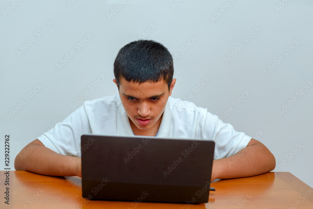Teenager with laptop sitting at table and studying at home. Fashion portrait of teen black hair handsome boy in office. Young businessman using a laptop. Teenager with laptop sitting at table and studying at home. Fashion portrait of teen black hair handsome boy in office. Young businessman using a laptop.