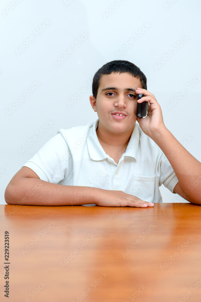 Teenager kid with phone in hand sitting at wood table in home.Teen boy with mobile phone used his smartphone on white background in school.Young businessman in office . Teenager kid with phone in hand sitting at wood table in home.Teen boy with mobile phone used his smartphone on white background in school.Young businessman in office .