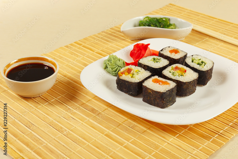 Sushi set, hiyashi wakame salad, soy sauce with ginger and wasabi on a bamboo mat close up. Sushi set, hiyashi wakame salad, soy sauce with ginger and wasabi on a bamboo mat close up.