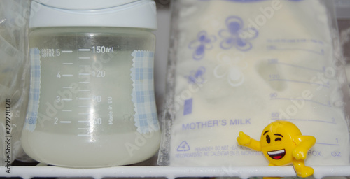 lot of frozzen breast milk in storage bags stored in the freezer and baby bottle with fresh expresed breastmilk photo