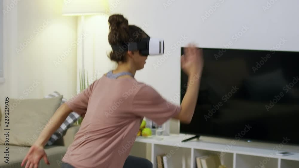 Tilt up of young woman wearing VR goggles and doing lunges with knee raises while training at home Tilt up of young woman wearing VR goggles and doing lunges with knee raises while training at home