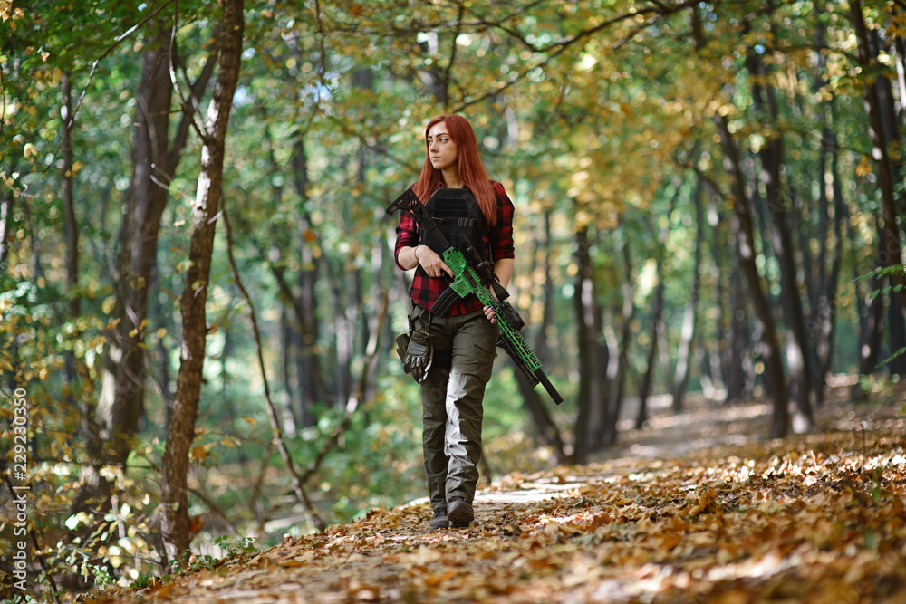 Cute girl with red hair and rifle in her hands on the background of trees