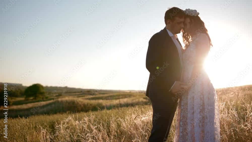 Caucasian bride and groom posing in the field with sunset sun, Moment of love and tender. Caucasian bride and groom posing in the field with sunset sun, Moment of love and tender.