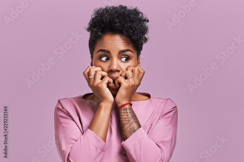 Emotions concept. Nervous emotional scared young lovely African American female stares at camera and opens mouth widely, notices phobia, expresses her fear against something, poses alone indoor photo