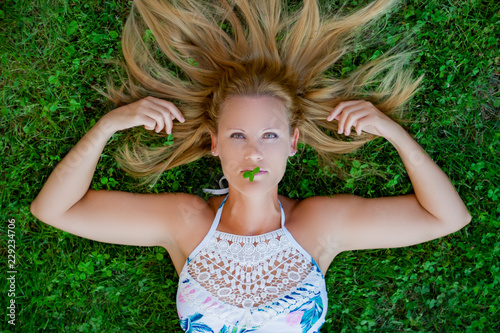 Girl lying on the grass with a clover on her lips