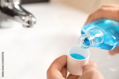 Fototapeta Naklejka Na Ścianę i Meble -  Man pouring mouthwash from bottle into cap in bathroom, closeup. Teeth care