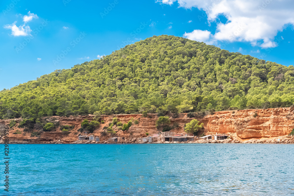 Ibiza, Sa Caleta beach, old fisherman’s sheds on the shore, beautiful red cliffs 
