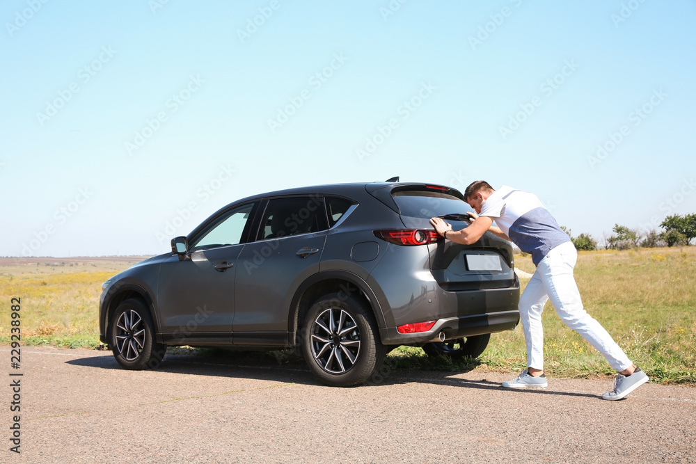 Man pushing broken car along country road Man pushing broken car along country road