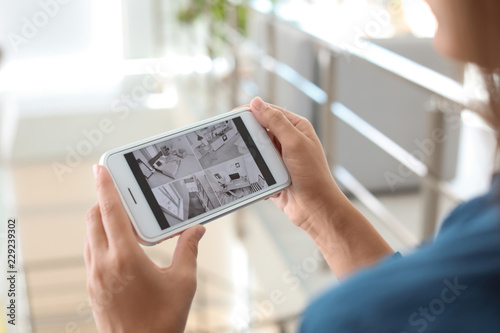 Woman monitoring modern cctv cameras on smartphone indoors, closeup