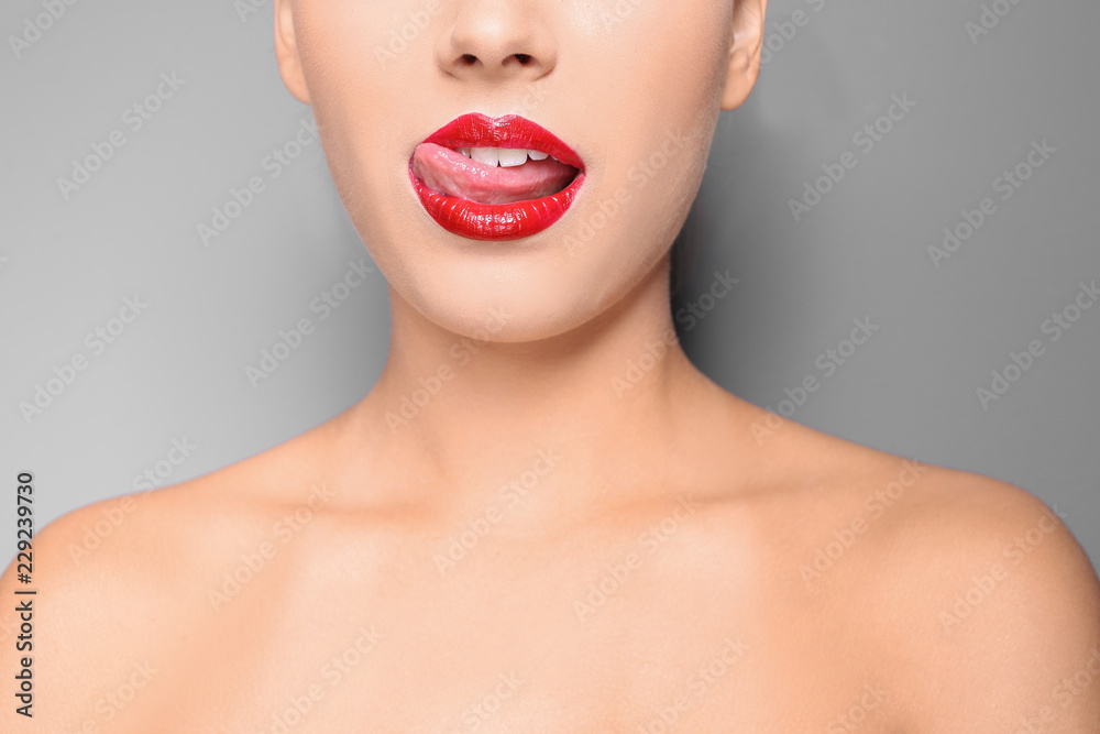 Naklejka premium Beautiful young woman with red glossy lips on gray background, closeup