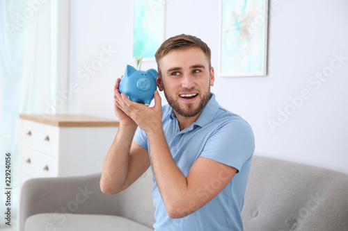 Young man with piggy bank on sofa in living room
