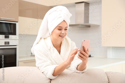Beautiful woman with hair wrapped in towel using smartphone at home