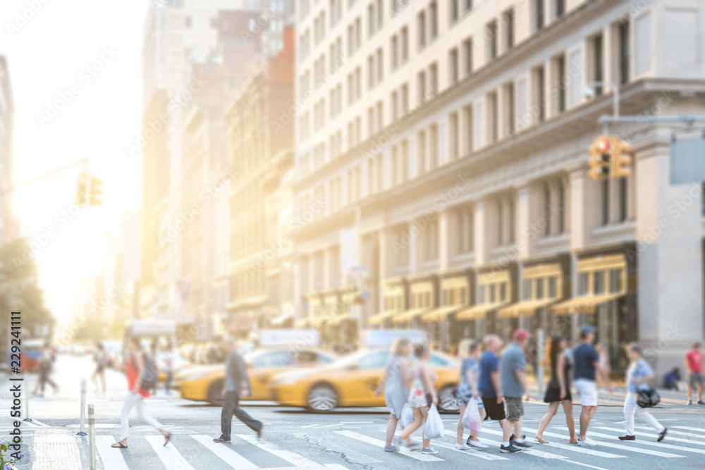 Crowds of anonymous people walking across an intersection on 5th Avenue in Manhattan New York City with colorful sunlight background