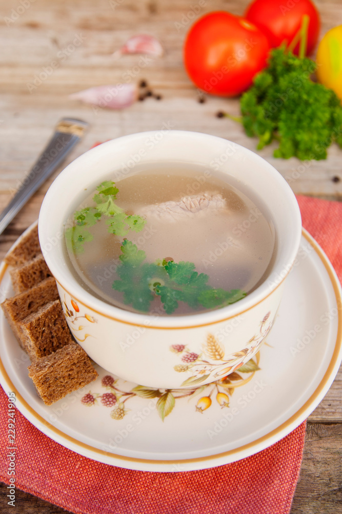 Clear beef broth, bouillon in white bowl and vegetables on wooden table. Rustic style. Clear beef broth, bouillon in white bowl and vegetables on wooden table. Rustic style.