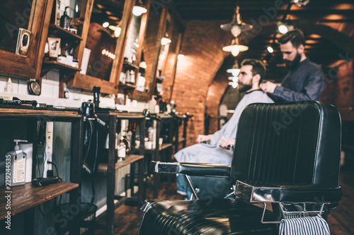 A picture of hairstylist standing on the back from his customer and putting cover on his client's shoulders.