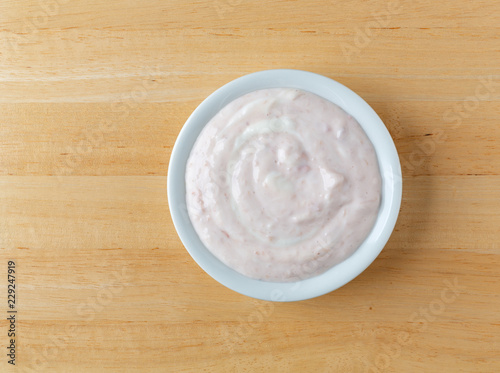 Top view of a bowl of strawberry rhubarb yogurt sweetened with honey on a wood table.