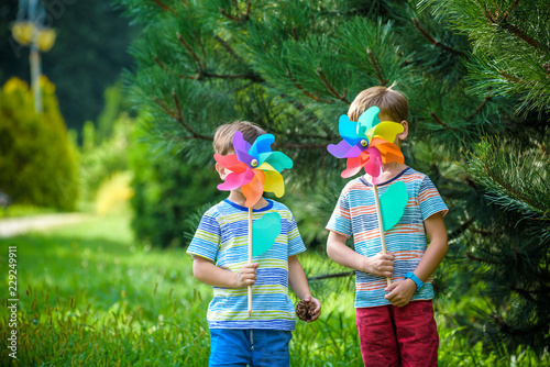 Two happy children playing in garden with windmill pinwheel. Adorable sibling brothers are best friends. Cute kid boy smile spring or summer park. Outdoors leisure friendship family concept