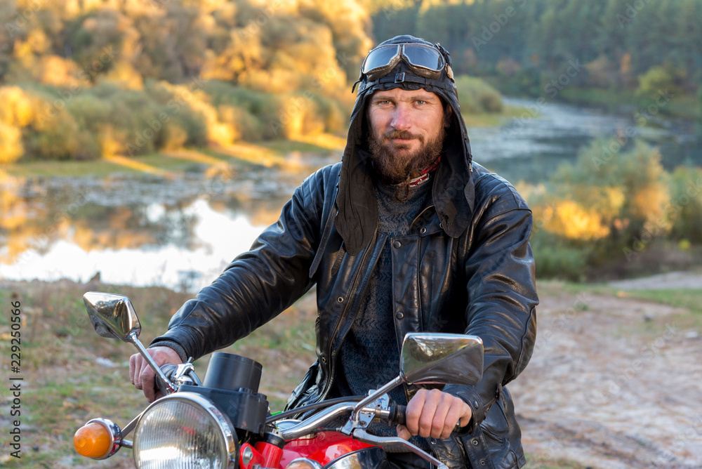 Biker in a leather jacket and helmet on a retro motorcycle in the forest