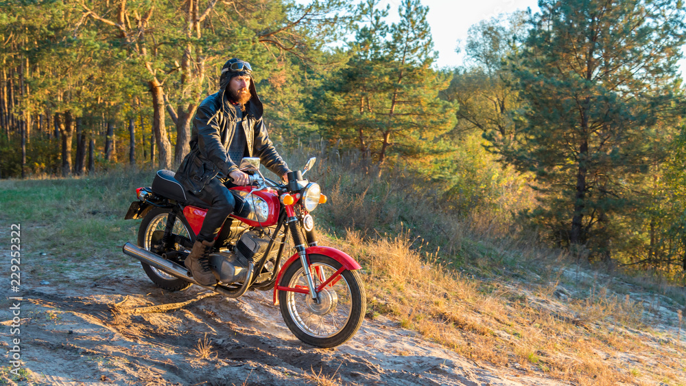 Biker in a leather jacket and helmet on a retro motorcycle in the forest