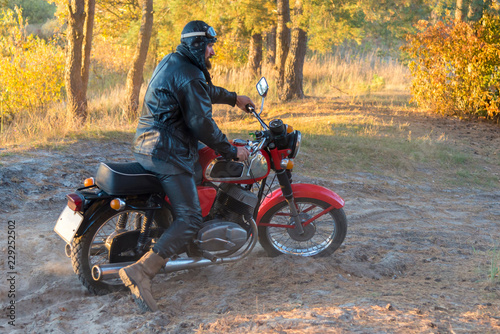 Biker in a leather jacket and helmet on a retro motorcycle in the forest © Pavlo