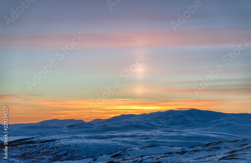 Very beautiful sunset at Scandinavian mountains - red orange sun beams coloring the white snow and blue sky, sun shines up as a laser beam
